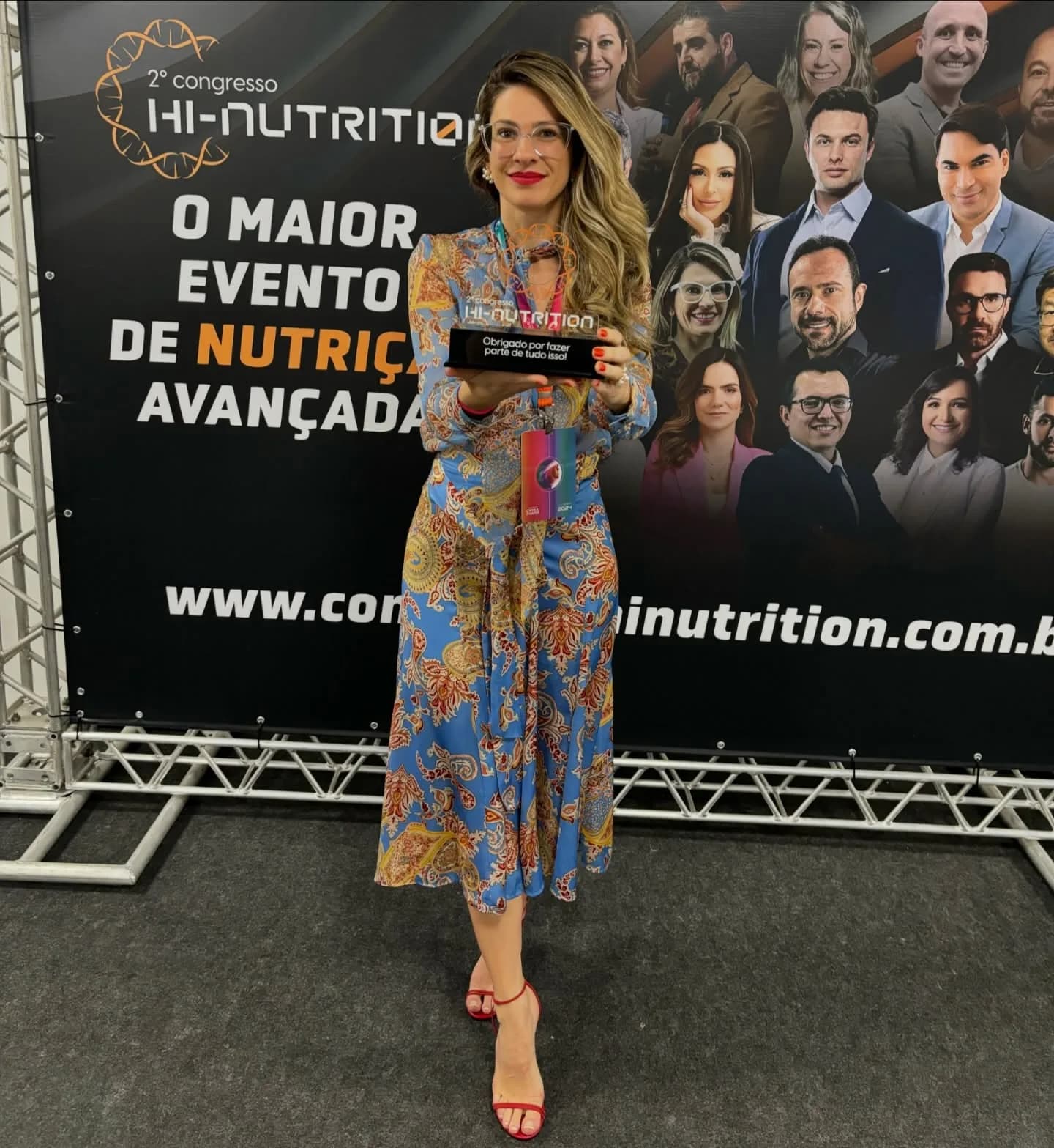 Luisa Wolpe com placa de reconhecimento diante do painel oficial de palestrantes do 2º Congresso Hi-Nutrition
